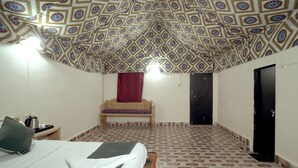 A room with a patterned ceiling, a bed, a bench, a door, and a tiled floor. - Experience the Best Jaisalmer Desert Safari & Luxury Camp Stay (Jaisalmer)