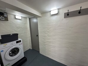 Un lavadero con una lavadora de carga frontal, una secadora y una puerta. Hay dos luces empotradas en la pared y un gancho negro.