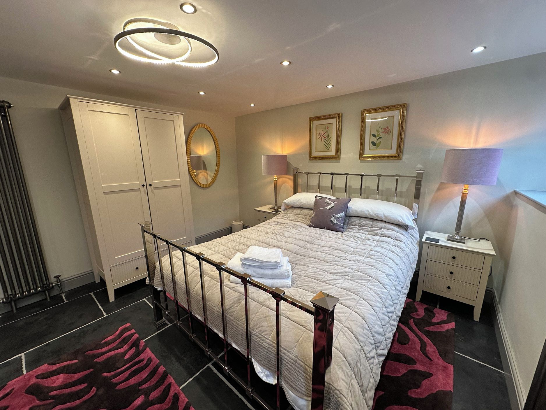 A hotel room with a bed, bedside tables, a wardrobe, a mirror, and a ceiling light fixture.