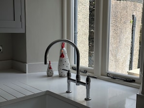 Eine moderne Küche mit weißer Arbeitsplatte, einem Edelstahlarmaturen und einem Fenster mit Blick auf eine Steinmauer.