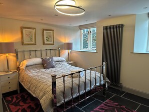 Ein Schlafzimmer mit einem Bett, Nachttischlampen, einem Fenster mit Vorhängen und gerahmten Bildern an der Wand.