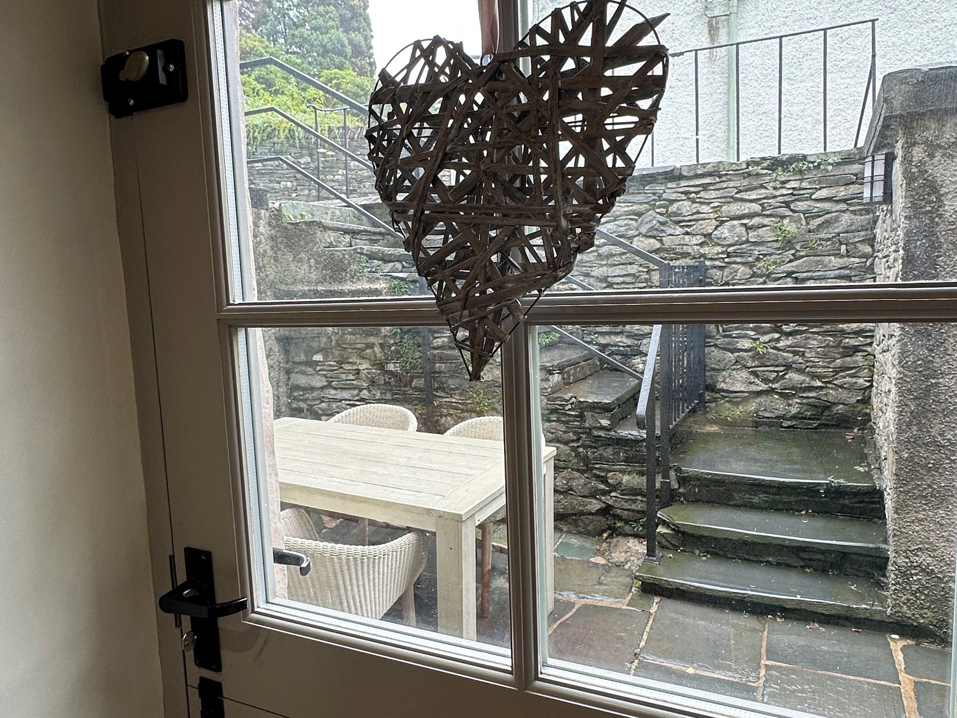 A window with a heart-shaped decoration, a stone staircase, and a wicker table and chairs outside.
