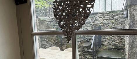 A window with a heart-shaped decoration, a stone staircase, and a wicker table and chairs outside.