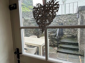 A window with a heart-shaped decoration, a stone staircase, and a wicker table and chairs outside. - La'al Kirkstone Brow (Ambleside)