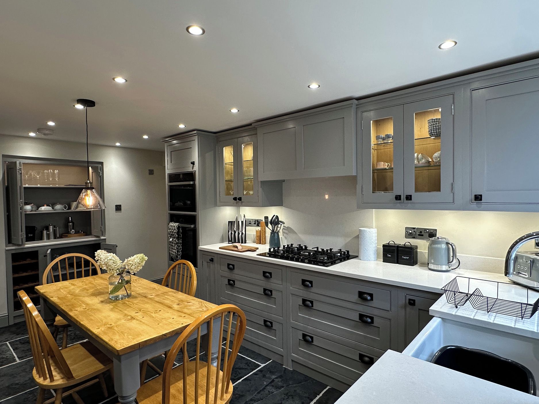 A modern kitchen with grey cabinets, a wooden dining table, and a built-in oven.