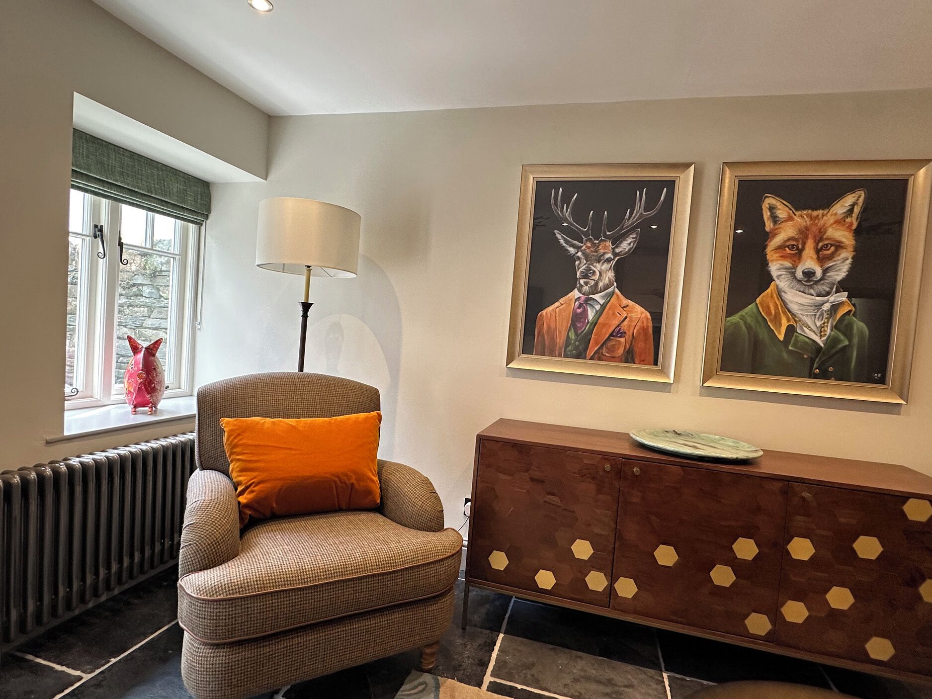 A room with a window, a chair, a lamp, a radiator, and two framed paintings on the wall.