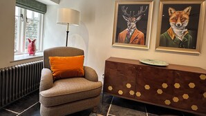 Um quarto com janela, uma cadeira, um abajur, um radiador e duas pinturas emolduradas na parede.