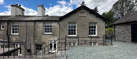 A two-story stone building with a gravel driveway and a metal staircase leading to the entrance.
