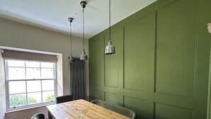 Ein Zimmer mit Holztisch, zwei Stühlen, einem Fenster mit Jalousien und einer grünen Wand.