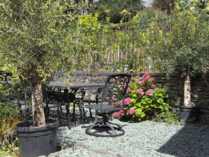 An outdoor seating area with a table and chairs, surrounded by a metal fence and various plants. - Kirkstone Brow (Ambleside)