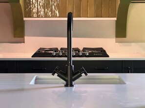 A kitchen with a black faucet, a white countertop, and a black stove with the brand name 'SMEG' visible. - Kirkstone Brow (Ambleside)