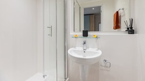 A modern bathroom with a glass shower enclosure, a white sink, and a mirror above the sink. - Student Only Centre Court (Nottingham)