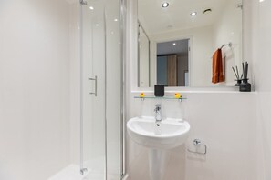 A modern bathroom with a glass shower enclosure, a white sink, and a mirror above the sink. - Student Only Centre Court (Nottingham)