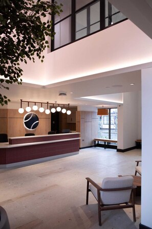 A modern reception area with a wooden reception desk, a large circular wall feature, and a seating area with a bench and chairs. - Student Only Centre Court (Nottingham)