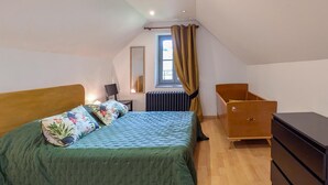 Ein Schlafzimmer mit Bett, Kommode, Stuhl, Heizkörper und einem fenster mit Vorhängen.