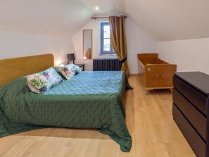 Ein Schlafzimmer mit Bett, Kommode, Stuhl, Heizkörper und einem fenster mit Vorhängen.