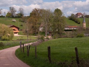 Ländliche Landschaft mit Feldweg, Holzzaun und Gebäuden im traditionellen Baustil.