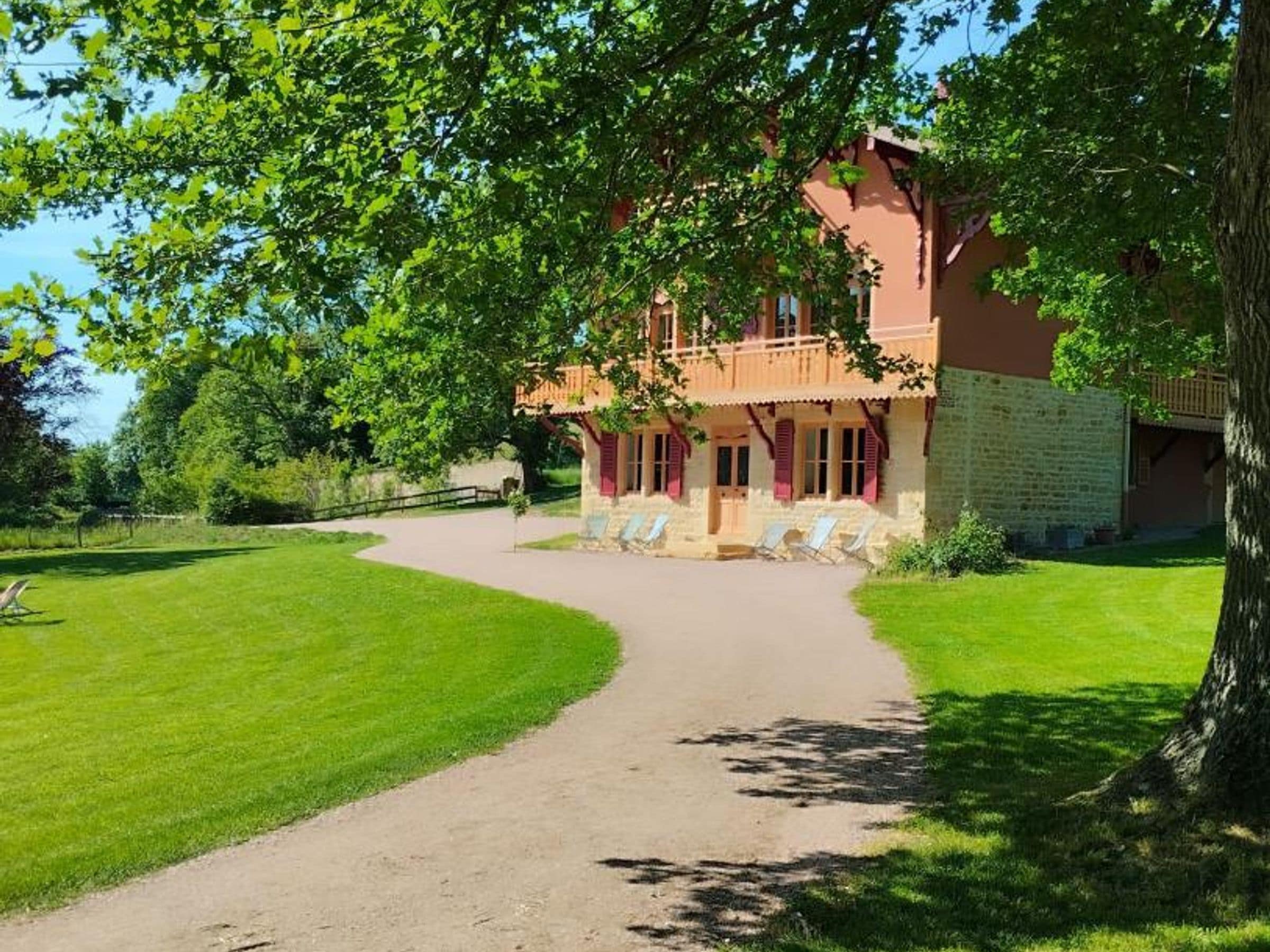 Un bâtiment à deux étages avec une allée pavée menant à un espace extérieur abrité, aménagé pour s’asseoir.