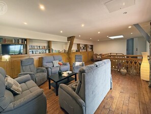 A spacious living room with multiple seating options, a wooden staircase, and a bookshelf filled with books. - Spacious house in the heart of the Loire - 15 guests (Pouilly-sous-Charlieu)