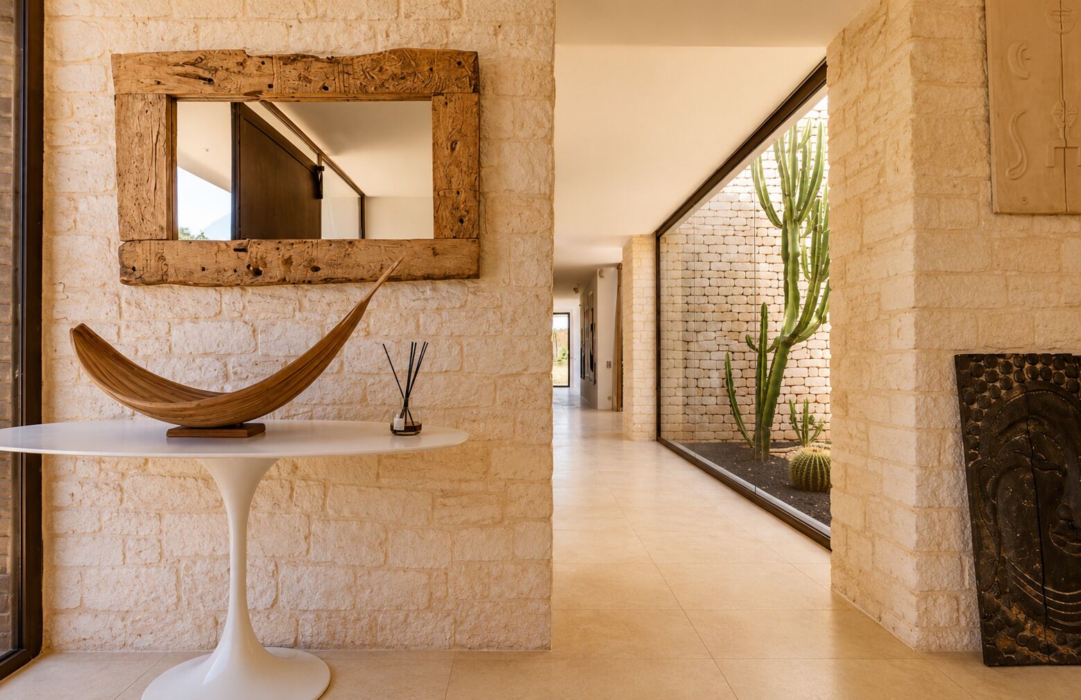 Un pasillo con una mesa blanca, un cuenco de madera, un espejo y una exhibición de cactus.