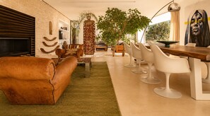 Ein modernes Wohnzimmer mit einer Ledersofa, einem Essbereich mit weißen Stühlen, einer großen Pflanze und einem Kamin.