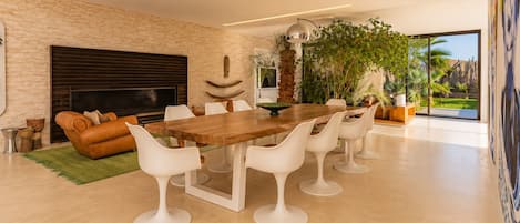 Una sala de estar moderna con chimenea, una mesa de comedor con sillas blancas y un ventanal con vistas al verdor.