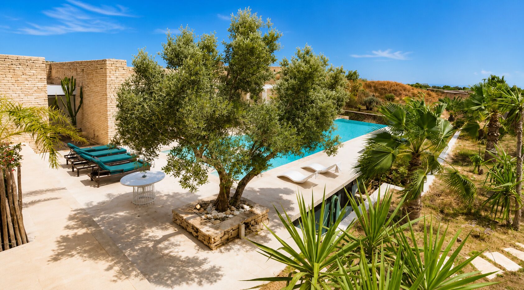 A poolside area with lounge chairs, a table, and a tree.