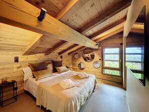 A cozy wooden cabin bedroom with a large bed, a small table, and a window with a view of the outdoors. - Stunning half-chalet in the village centre - 8 guests (Combloux)