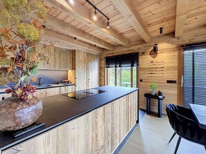A modern kitchen with wooden cabinetry, a central island, and a dining area with a black chair. - Stunning half-chalet in the village centre - 8 guests (Combloux)