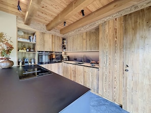 A modern kitchen with wooden cabinetry, a central island, and built-in appliances. - Stunning half-chalet in the village centre - 8 guests (Combloux)