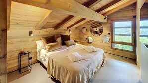 A wooden cabin bedroom with a bed, pillows, a bedside table, and a window with a view. - Stunning half-chalet in the village centre - 8 guests (Combloux)