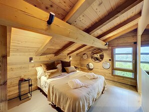 Ein Schlafzimmer einer Holzhütte mit einem Bett, Kissen, einem Nachttisch und einem Fenster mit Blick.