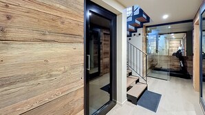 A modern interior with a wooden wall, a glass door, and a staircase with a metal railing. - Stunning half-chalet in the village centre - 8 guests (Combloux)