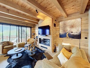 A cozy living room with a fireplace, a television, and a large window with blinds. - Stunning half-chalet in the village centre - 8 guests (Combloux)