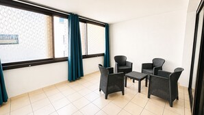 Um quarto com soalho em mosaico, janela com cortinas e um espaço de estar com mobiliário de vime.