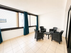 Ein Zimmer mit Fliesenboden, einem fenster mit Vorhängen und einer Sitzecke mit Rattanmöbeln.
