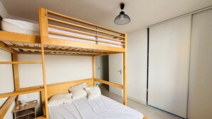 Uma cama beliche com estrutura de madeira, uma cama de solteiro embaixo e um guarda-roupa à direita.