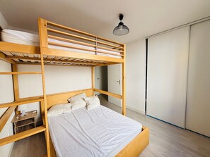 Ein Stockbett mit Holzrahmen, ein Einzelbett darunter und ein Kleiderschrank zur Rechten.