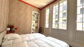 Quarto com uma cama grande, uma estante de livros e uma janela com vista para edifícios.
