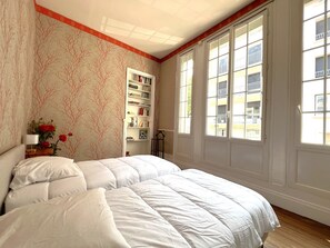 A bedroom with a large bed, a bookshelf, and a window with a view of buildings.
