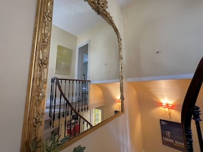 A staircase with a wooden railing, a large ornate mirror, and a poster on the wall.