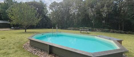 A rectangular swimming pool with a stone border, surrounded by a grassy area and trees.
