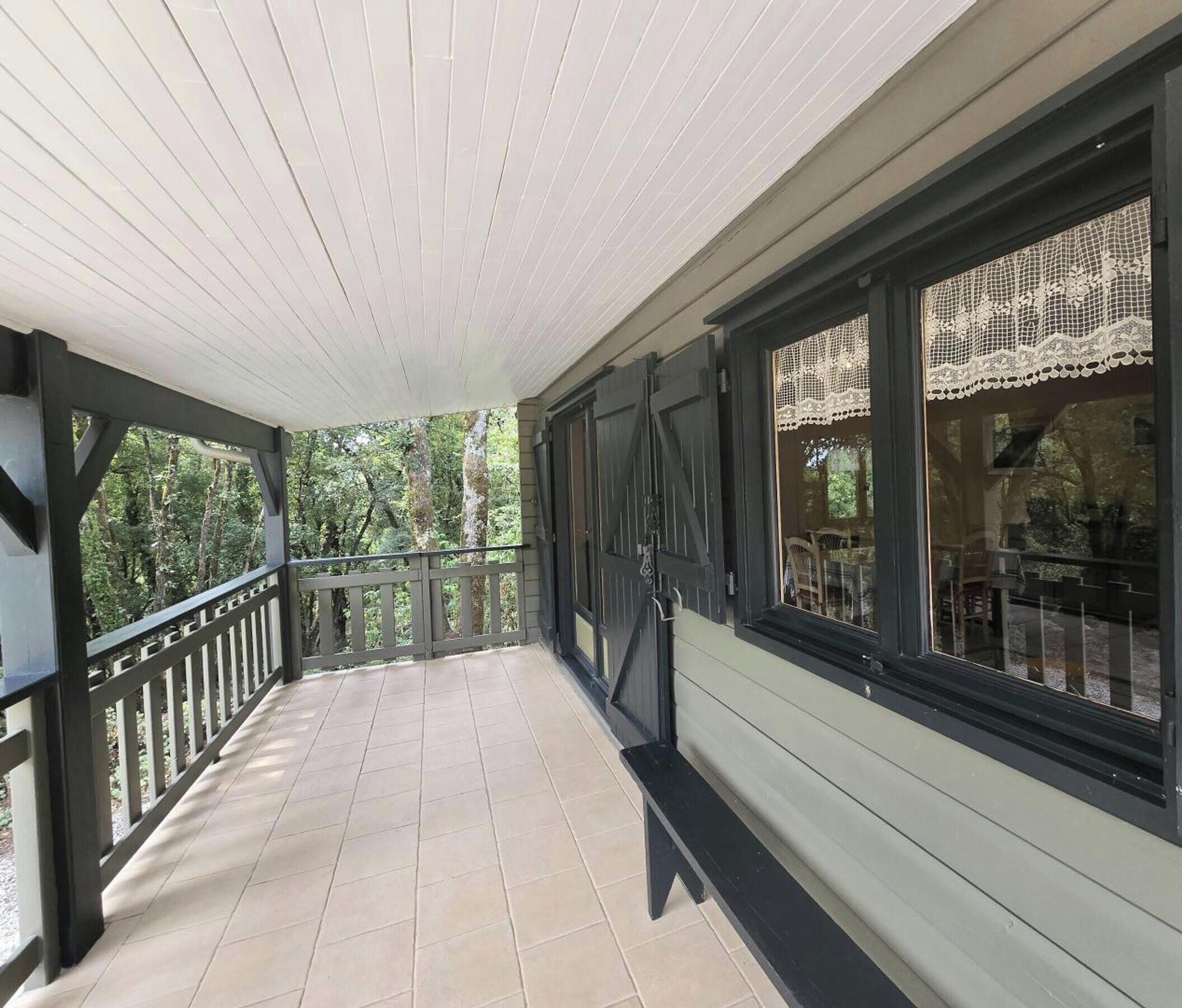 A covered porch with a tiled floor, black railings, and large windows with lace curtains.