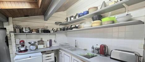 A kitchen with white cabinets, a white countertop, a toaster, a kettle, and various pots and pans on shelves.