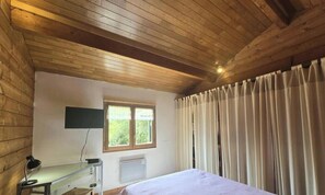 A room with a wooden ceiling, a bed, a desk with a lamp, a window with curtains, and a wall-mounted TV. - Private chalet, pool and AC near Castelnaud - 4 guests (Castelnaud-la-Chapelle)
