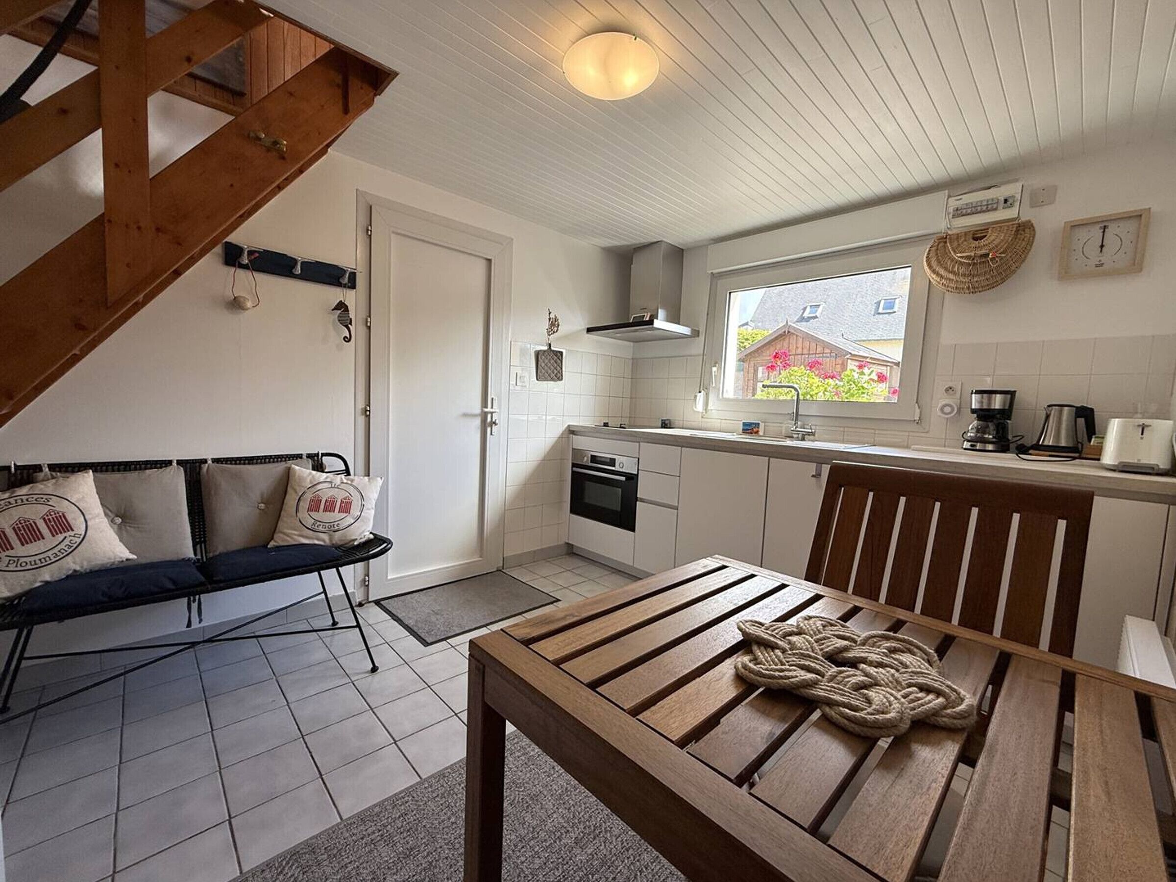 A compact kitchen with a dining area, a wooden table, and a view of the outside through a window.
