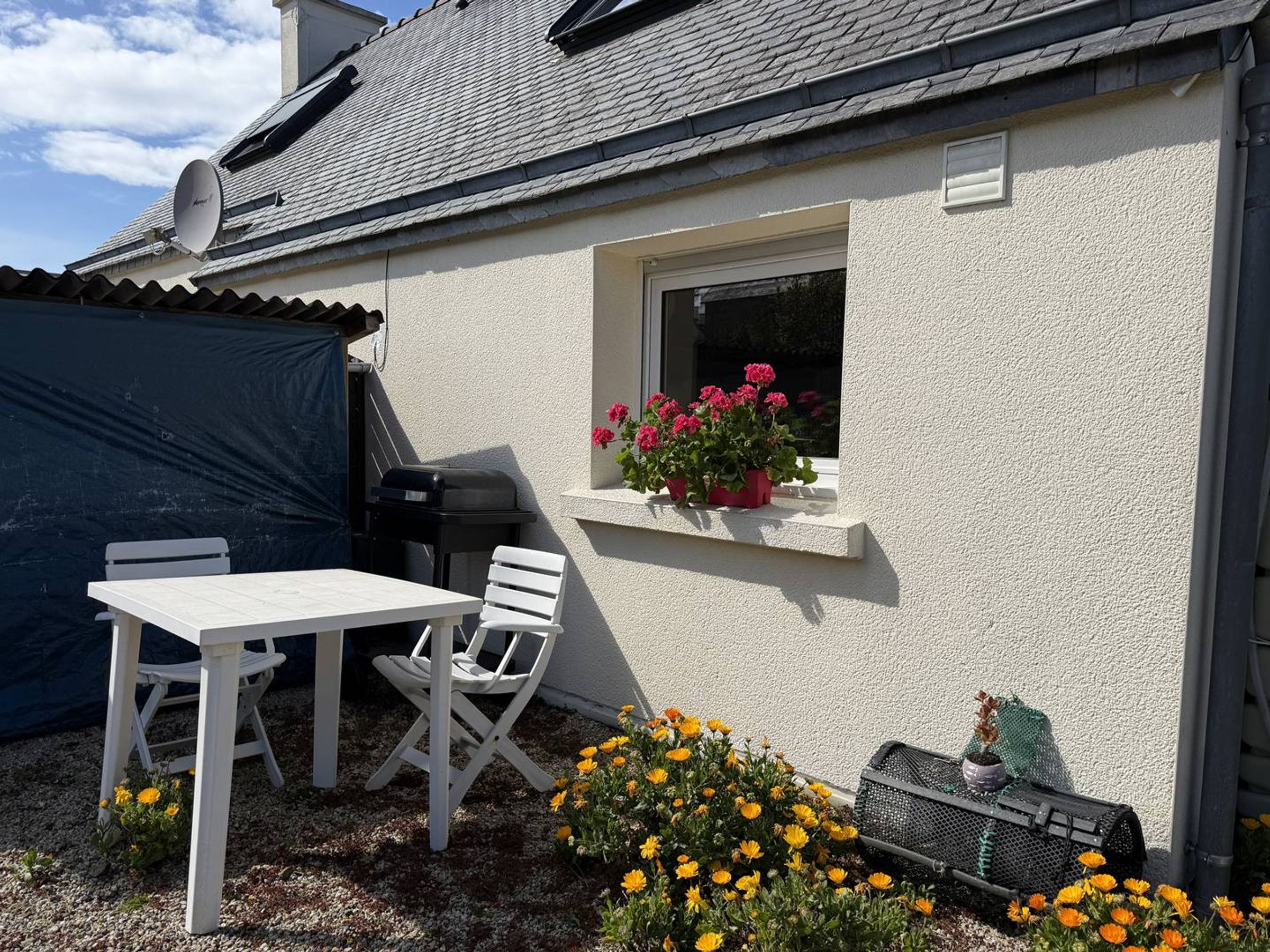 Eine Terrasse mit einem weißen Tisch und Stühlen, einem Grill und Blumentöpfen.