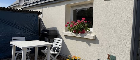 Eine Terrasse mit einem weißen Tisch und Stühlen, einem Grill und Blumentöpfen.