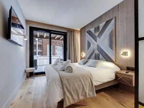 Une chambre moderne avec un grand lit, un mur d’accent en bois et une vue sur un balcon enneigé.