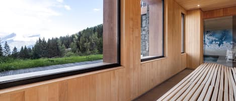 A modern interior with wooden paneling, large windows offering a view of a forest and mountains, and a bench along the wall.